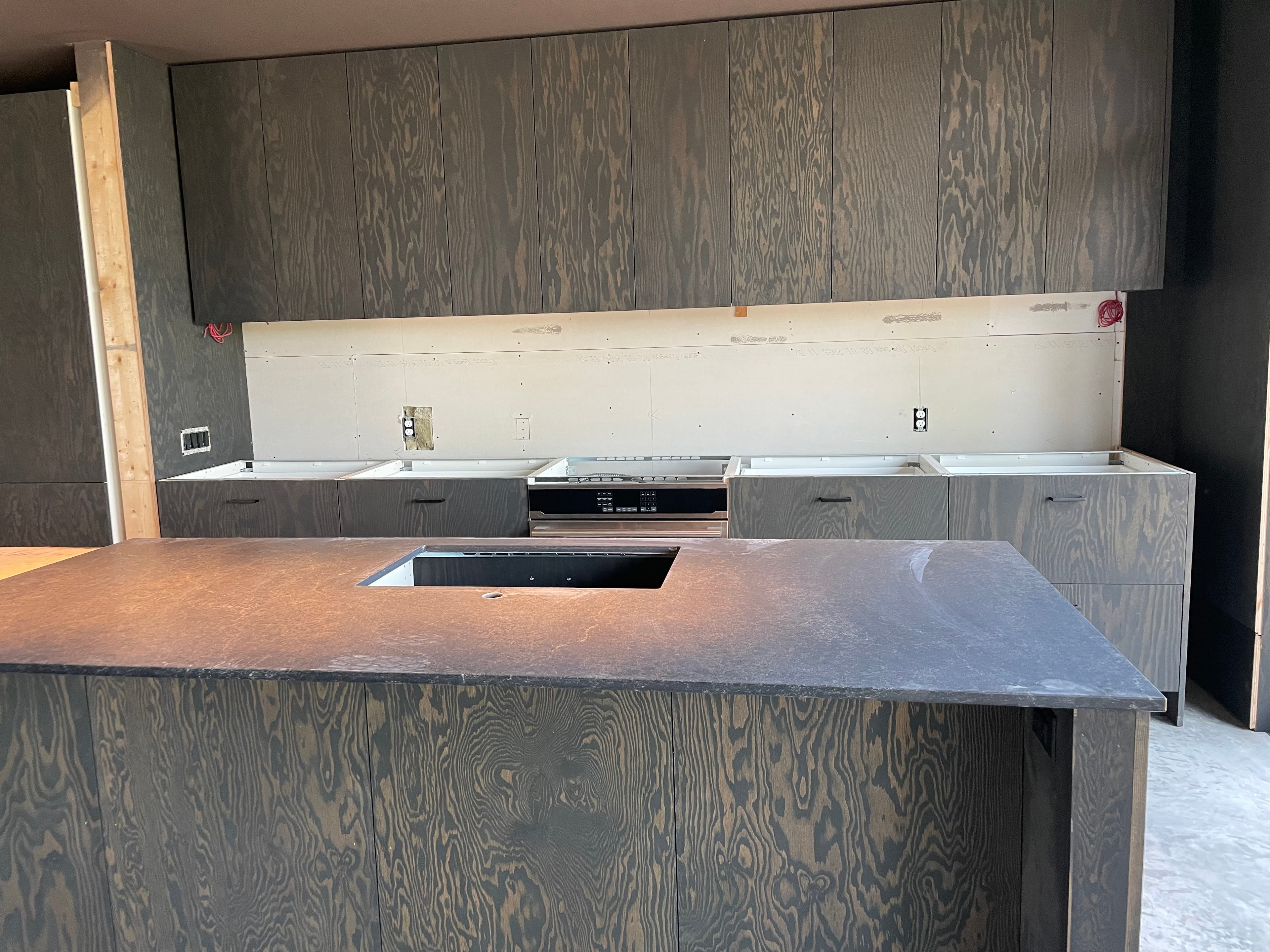 Sunroom addition — custom kitchen under construction with dark cabinetry and stone island